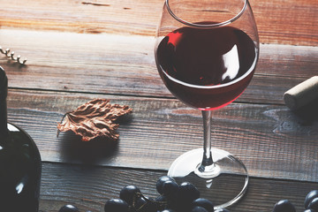 A glass of red wine with grapes and a bottle on a wooden table.