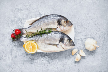 Fresh uncooked dorado or sea bream fish with lemon over gray background. Top view, copy space.