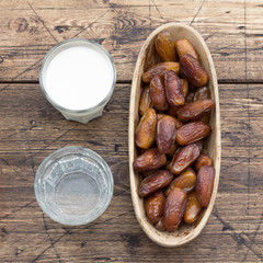 Dried dates fruits on a branch, a glasses of water and milk on a wooden table. Traditional fast breaking, Muslims evening meal during holy Ramadan