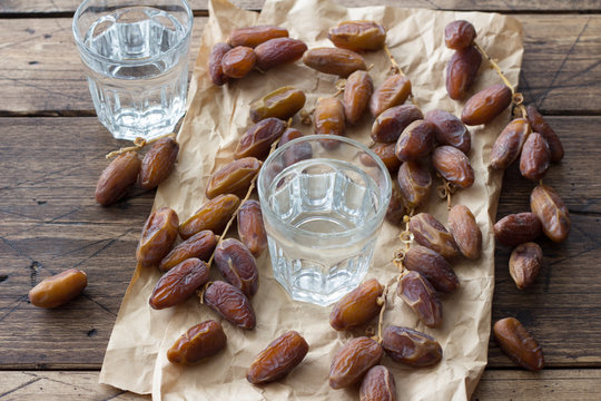 Dried dates fruits on a branch and a glass of water on a wooden table. Traditional fast breaking, Muslims evening meal during holy Ramadan