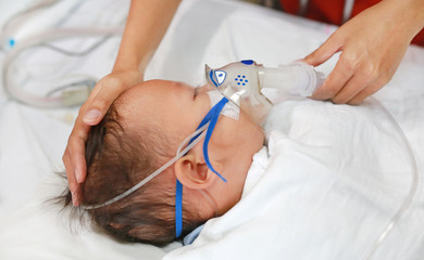 Toddler boy using nebulizer to cure asthma or pneumonia disease . Sick baby boy rest on patients...
