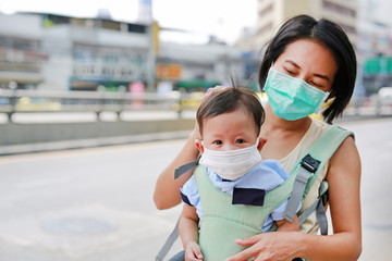 Fototapeta na wymiar Asian mother carrying her infant baby by hipseat outdoor with wearing a protection mask against PM 2.5 air pollution in Bangkok city. Thailand.