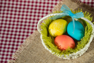 Easter colored eggs in a basket on a canvas napkin and checkered tablecloth.