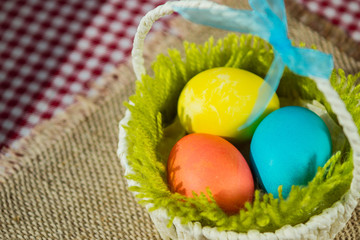 Easter colored eggs in a basket on a canvas napkin and checkered tablecloth.