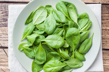 Fresh spinach leaves in bowl on rustic wooden table.