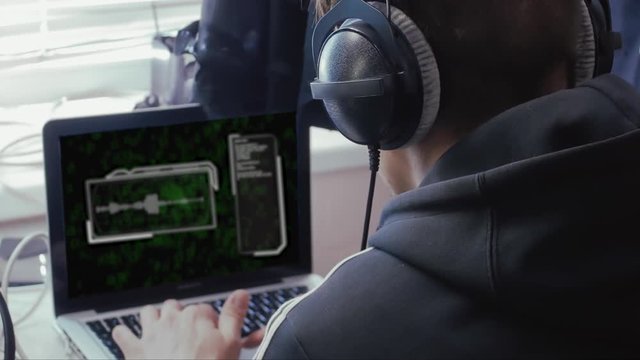 The hacker works on a computer with a sound chart and green binary symbols. The man in the headphones analyzes the voice code. Programming audio coding in the office or at home