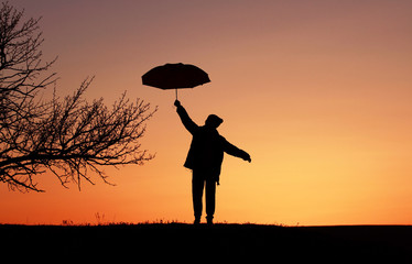 Silhouette boy child with umbrella on sunset background