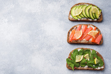 Open sandwiches with spinach and avocado salmon on a grey table. Copy space