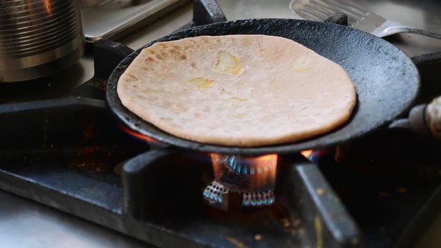 Preparing Indian aloo paratha in a frying pan on gas stove, close-up in slow motion