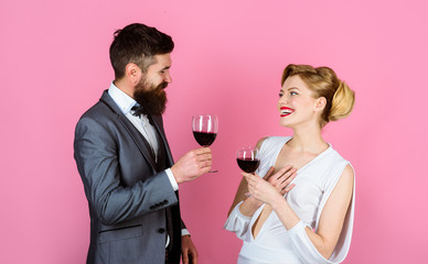 Woman in white dress and handsome man in suit dating in restaurant. Couple holds glass of red wine. Happy couple drinking red wine and flirting. Beautiful couple with glasses of red wine in restaurant