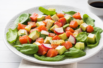 Poke Hawaiian salad with salmon, avocado spinach and vegetables in a plate on a white table.