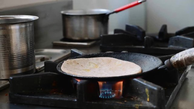 Chef repeat Indian aloo paratha to frying pan with metal spatula. Close-up view.