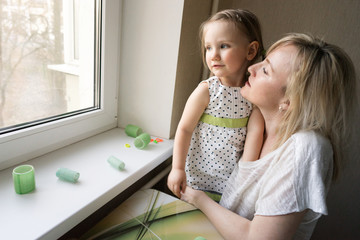 Mom and daughter 3 years old sitting at the window