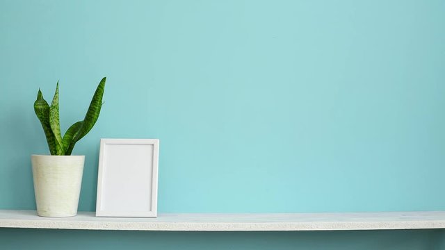 Modern room decoration with Picture frame mockup. White shelf against pastel turquoise wall with hand putting down potted snake plant.
