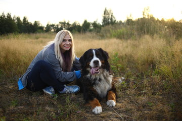 Young woman walking with Bernese Mountain Dog on the summer field