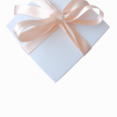 White gift box wrapped with rose beige colour ribbon tied in a bow 