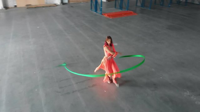 Ballet training indoors. Young woman performing circus elements with an acrobatic ribbon