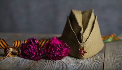 Military cap, carnations, Saint George ribbon on a wooden surface.