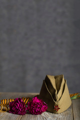 Military cap, carnations, Saint George ribbon on a wooden surface.