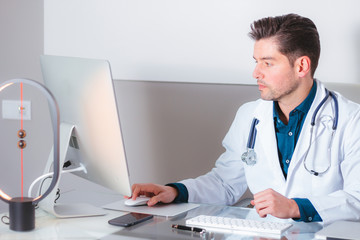Young attractive doctor working with computer in modern hospital office.