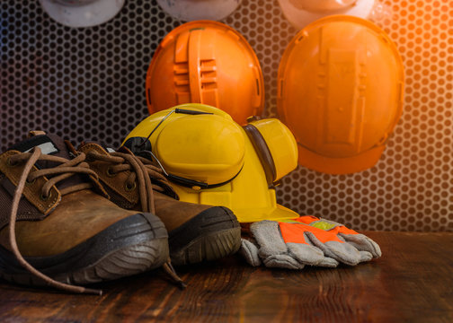 Personal protective equipment in the workplace is placed on a wooden table,with a safety helmets hanging in the background.