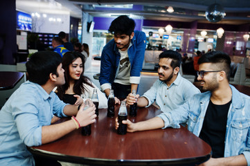 Group of stylish asian friends wear on jeans sitting at table and drink soda from bottles in club.