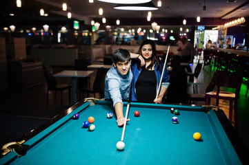 Stylish asian couple wear on jeans playing pool billiard on bar.