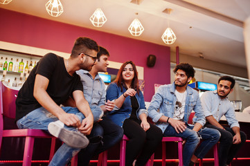 Group of stylish asian friends wear on jeans sitting at chairs against bar in club and chatting together.