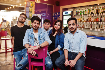Group of stylish asian friends wear on jeans sitting at chairs against bar in club.