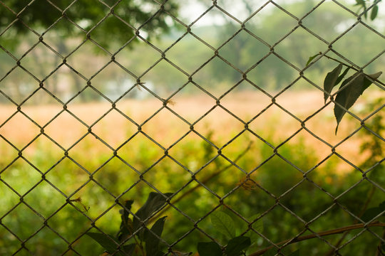 Fence made of wired steel designed in colander with blurred rural football field in background