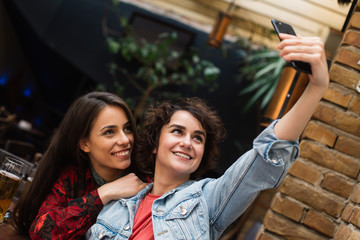 Two girls taking selfies from above. Girls taking selfies at a coffee shop. Two friends posing for a selfie.
