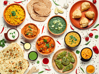 Indian cuisine dishes: tikka masala, dal, paneer, samosa, chapati, chutney, spices. Indian food on white wooden background. Assortment indian meal top view or flat lay.