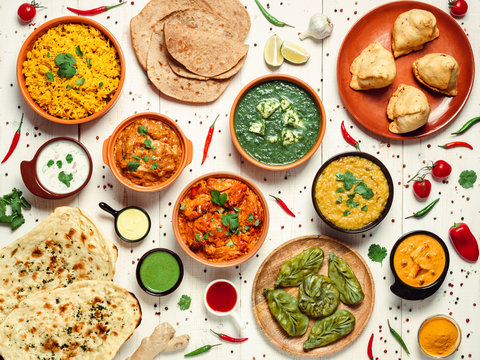 Indian cuisine dishes: tikka masala, dal, paneer, samosa, chapati, chutney, spices. Indian food on white wooden background. Assortment indian meal top view or flat lay.