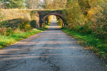 Fototapeta na wymiar Old arched overpass over the road. Yellowed trees in autumn along the road.