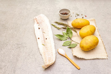 Raw young potatoes and frozen hake fillets. Ingredients for fish and chips. Spices and herbs on a stone background.