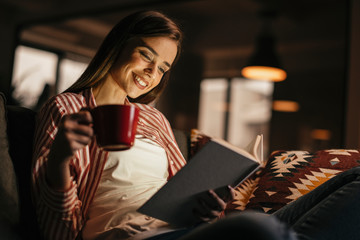 Girl having a cup of coffee while reading a book. Woman reading a book on the couch.