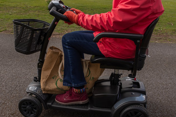 A side on shot of an elderly lady in a red coat enjoying the freedom of an electric mobility scooter, from the shoulders down