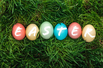 top view of painted multicolored eggs with Easter word on green grass