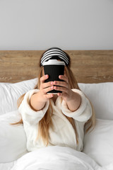 Sleepy woman with cup of hot coffee sitting in bed
