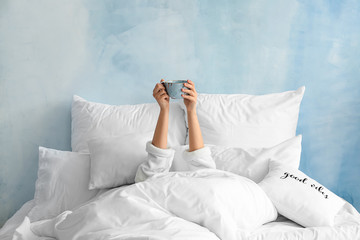 Young woman with cup of hot beverage lying in bed - obrazy, fototapety, plakaty