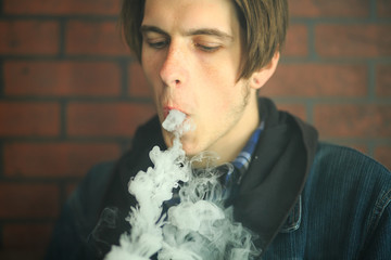 Vape teenager. Portrait of young handsome guy smoking an electronic cigarette in the bar. Bad habit...