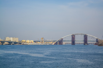 Naklejka premium View of Dnieper river and the bridge from the coast of Kiev. Modern big city. Beautiful spring landscape