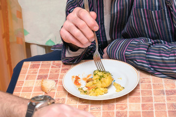 The man at the table in the kitchen eating potatoes