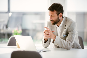 Businessman sitting looking at his laptop. Businessman working in the office on his laptop. Stylish businessman working on a project in the office thinking about future