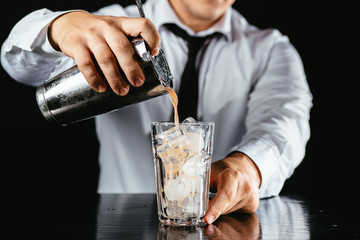 Barman makes an orange cocktail. Orange cocktail on a black counter, black background. Cocktail poured from a shaker. 
