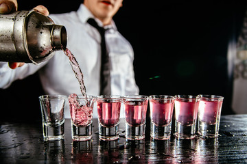 Barman making shots. Barkeeper pouring pink liquid. Bartender makes pink alcoholic shots.