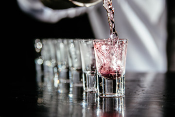 Barman making shots. Barkeeper pouring pink liquid. Bartender makes pink alcoholic shots.