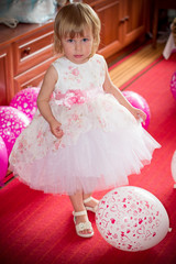 A little fair-haired girl, a child with blue eyes, dressed in a pastel pink dress, celebrates her birthday  