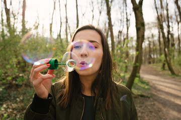 Young woman blowing soap bubbles in the woods.