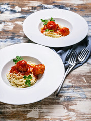 Vertical shot meatballs in tomato sauce with spaghetti on large white plates